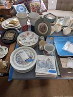 Assorted ceramic plates, framed tiles, mugs and goblet-style mugs arranged on table