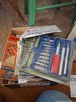 Open box showing plastic-cased hobby knife set, books, assorted items