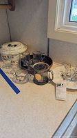 Group view of Hall's dish lid, egg tray, glass mugs and creamers on countertop