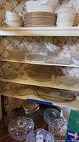 Stacked white plates and bowls, clear glass serving bowls and platter on shelves
