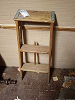 wooden two-step ladder with metal corner plates standing upright against wall