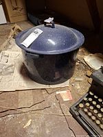 Blue speckled enamel stock pot with lid on basement floor, partial view of typewriter nearby