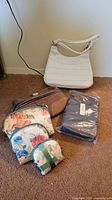All bags laid out: white handbag, three floral pouches, dark cosmetic pouch, sealed men’s travel bag