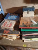 Overview of stacked LPs, 45s in sleeves, and blue-lid storage box on table