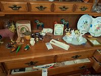 Overview of shelf showing cast iron dog doorstop, Dala horses, porcelain plates, bunny group, small vases and multiple miniature figurines