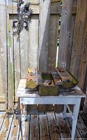 Full lot view: tackle box on table, contents visible, two rods leaning nearby