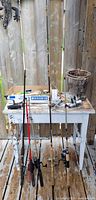 Full view of five rods with reels, tackle on table and minnow trap