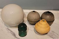 Group shot of milk glass globe, two aluminum lightning-rod globes, cream bakelite ball and green Brookfield insulator