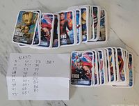 Stacks of Marvel Loblaws trading cards with handwritten list of missing numbers; visible cards include Baby Groot, Inferno, Thor