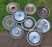 All nine vintage Ford hubcaps laid out on grass showing designs, size and wear