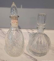 Both crystal decanters side by side showing shapes, stoppers, and tax seal