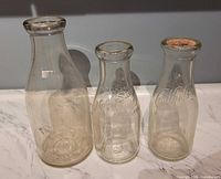 Three embossed glass milk bottles including Price's, North Side Dairy, Caulfield's (with cap)