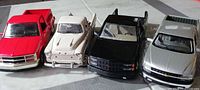 Front view of four Chevrolet die-cast pickups in red, white, black and silver