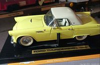 Left side view of yellow 1955 Ford Thunderbird model on black base