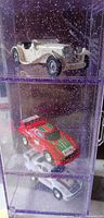Close view of top and middle shelves showing cream roadster and red rally car inside case