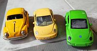 Front view of three Beetle cars: classic dark yellow, pale yellow coupe, bright green coupe