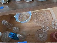 Nine assorted glass items including perfume bottles, ruffled bowl and pressed glass dishes inside wooden cabinet