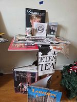 Overall lot view of books, magazines, mug, figure, tea towel and postcards