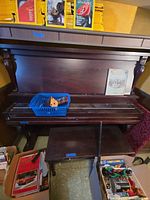 Front view of Doherty upright piano with bench and basket of sheet music
