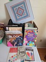 All items grouped: framed quilt, books, fabric bundle, patterns in tote