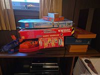 Stacked boxes showing LEGO City 7726, Tonka Motorized Power, Clue, small orange game, and loose track parts
