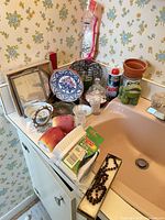 Overview of mixed lot on vanity showing plate, bowls, frames, frog planter, terracotta pot, wire basket, glassware, cleaning can