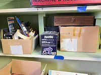 Shelf with boxed SuperLine inflator, cardboard box of masking tape and drill bits, wooden storage box