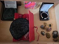 Drawer view showing etched glass plaque, red wallet, black beaded clutch, bracelet box, array of brooches