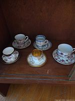 Five assorted porcelain teacup and saucer sets on shelf