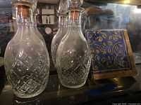 Two of the three diamond-cut decanters with corked glass stoppers beside packaged blue-and-gold napkins