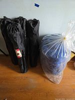 Three black carry bags for folding chairs and blue mattress in plastic bag