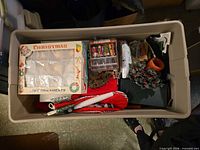 Plastic tote containing ornaments box, stockings, candles, greenery and small décor