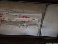 Stack of assorted folded linens showing floral print placemats, embroidered napkins, white damask cloth