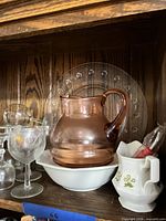 shelf with pink glass pitcher, clear charger plate behind, wine glasses, white bowl, ceramic creamer