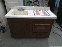 Front view of wooden play kitchen showing sink, stovetop, cabinet and drawer