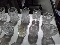Overhead view of fifteen clear pressed glass toothpick holders displaying varying patterns