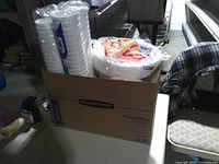 Box with stack of clear plastic cups and packaged plates visible