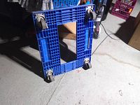 Top view of blue plastic dolly showing grid deck and four swivel casters