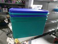 Three stacked teal totes with blue lids on table
