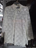 Front view of cream lace blouse hanging on hanger