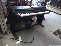 Full view of digital piano on stand with pedals and power cord