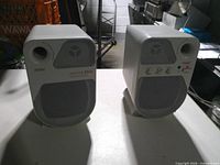 Front view of both speakers showing grilles, ports, model marking