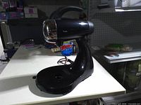 Front view of black Sunbeam Mixmaster base showing chrome logo cap and platform