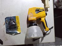 Front view of Wagner Pro sprayer with cup and sealed Optimus Stain Tip package