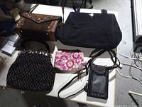 Five purses on table including brown clutch, black tote, black beaded handbag, floral wristlet, black crossbody phone purse