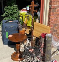 Group shot of entire lot at garage entrance showing table, plant stand, rolled rugs, coat rack, umbrella stand with umbrellas