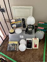 Overview showing boxed Coleman lanterns, table lamps, flashlight, lantern, radio, screwdriver set, diffusers