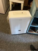 Front view of Danby white portable dehumidifier next to cabinet