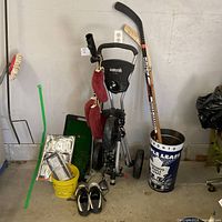 Full lot showing push cart, clubs, putting mat, bucket, shoes, hockey sticks in bin