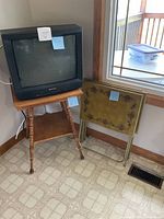 Hitachi CRT TV on wooden stand beside three stacked metal folding trays